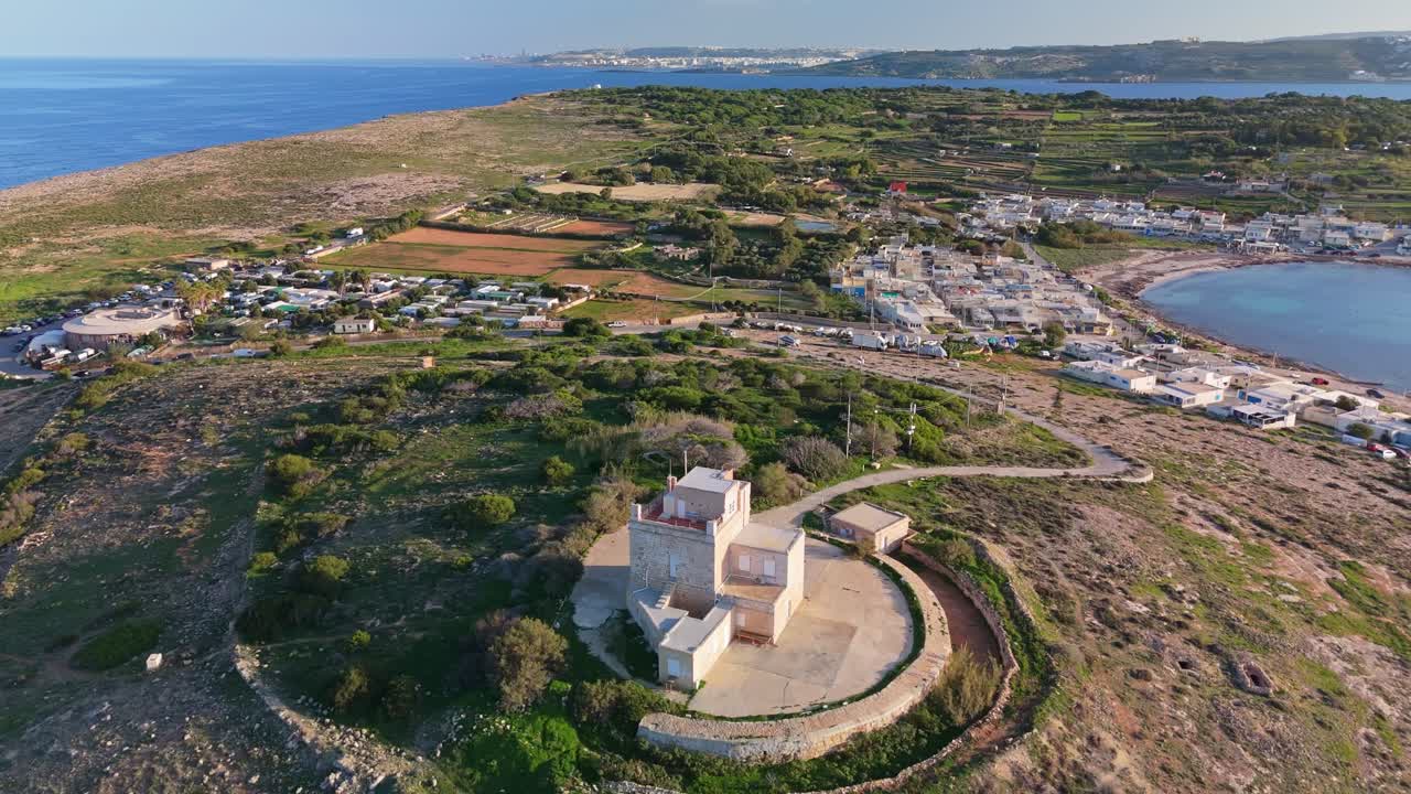 Vista orbitale di drone della Torre Bianca a Mellieha, Malta, che evidenzia la sua architettura medievale, la struttura restaurata e la pittoresca costa mediterranea circondata da villaggi e paesaggi naturali