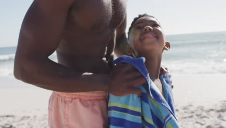 Sonriente-Padre-Afroamericano-Secando-A-Su-Hijo-En-La-Playa-Soleada