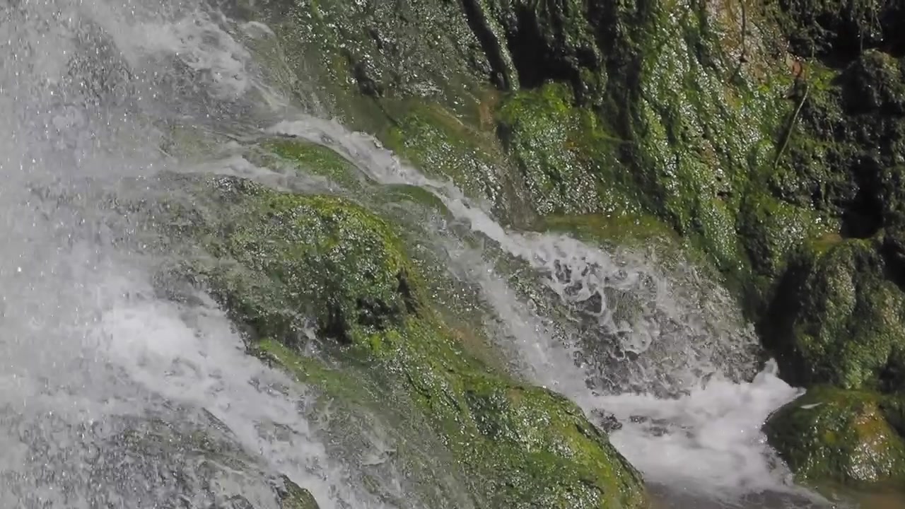 Acqua impetuosa che scende a cascata su rocce verdi e muschiose in natura