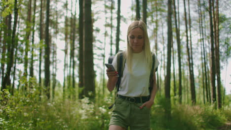 attractive woman relax in forest and using smartphone outdoors. woman hiking in the forest and typing message on smartphone. solo female hiker using smart phone.