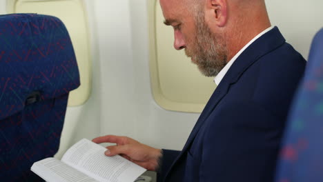 a business man with a beard reading a book on a passenger plane airliner