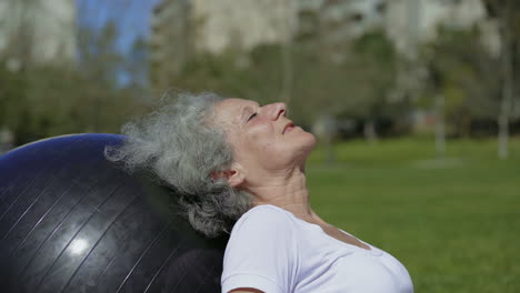 smiling senior woman resting after workout near gym ball.