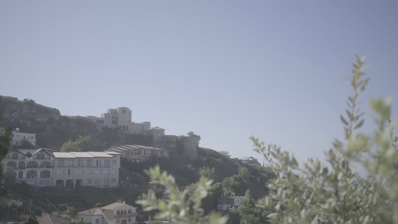 tomada del antiguo castillo de kruje, albania, filmada desde detrás de las plantas en un día soleado y brillante con cielo azul y sin personas en primer plano.