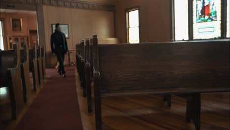 pastor in black suit walking in church sitting in pew in cinematic slow motion