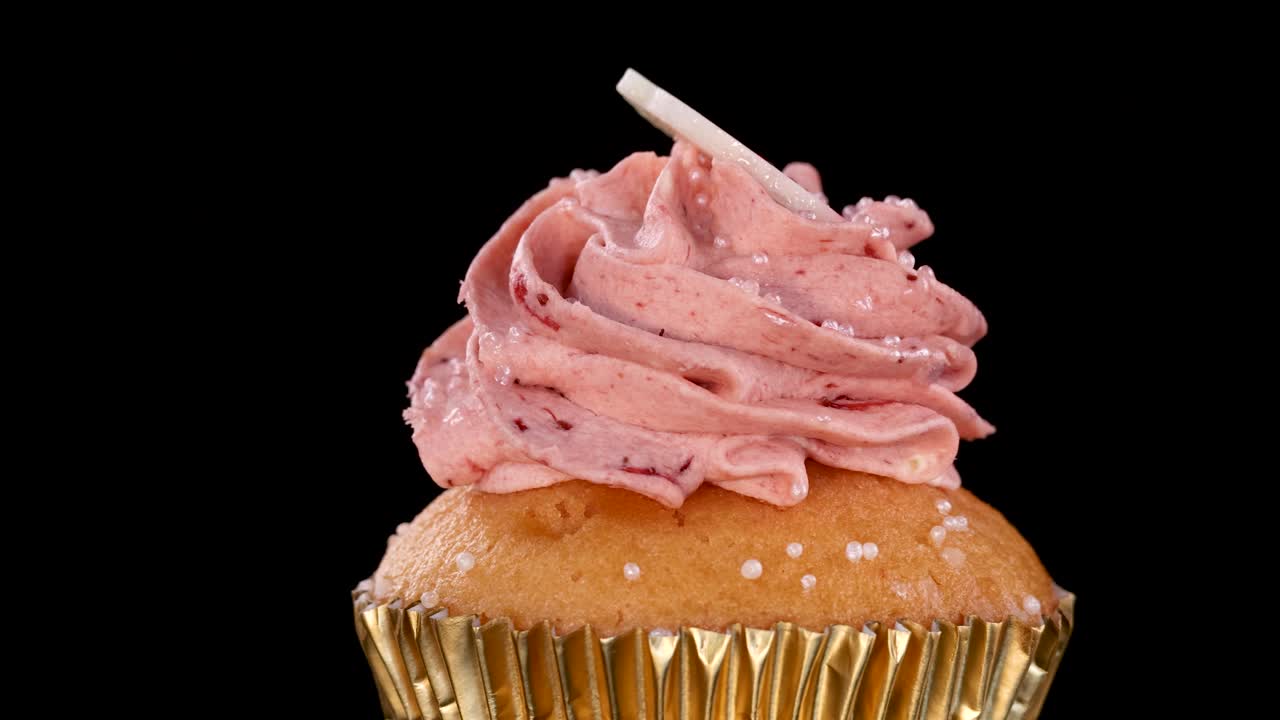 Un singolo cupcake alla fragola con glassa rosa e decorazioni ruota dolcemente su uno sfondo nero uniforme sotto un'illuminazione da studio omogenea, evidenziandone la texture e i dettagli.
