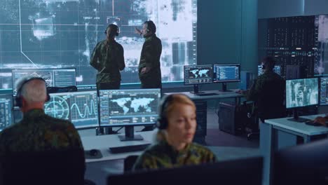 military surveillance team of officers locked a target on a vehicle from a satellite and monitor it on a big display in office for cyber operations for managing security and army communications.