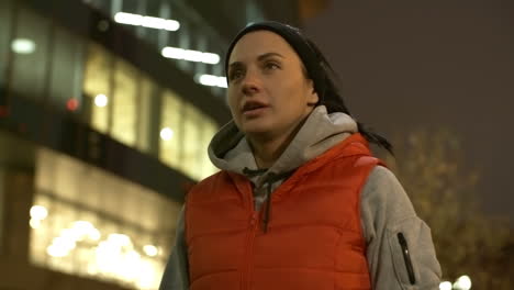 camera focuses on the face of a woman in sportswear who takes a break while running in the city at night