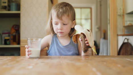wholesome shot of healthy caucasian child drinking milk and eating banana