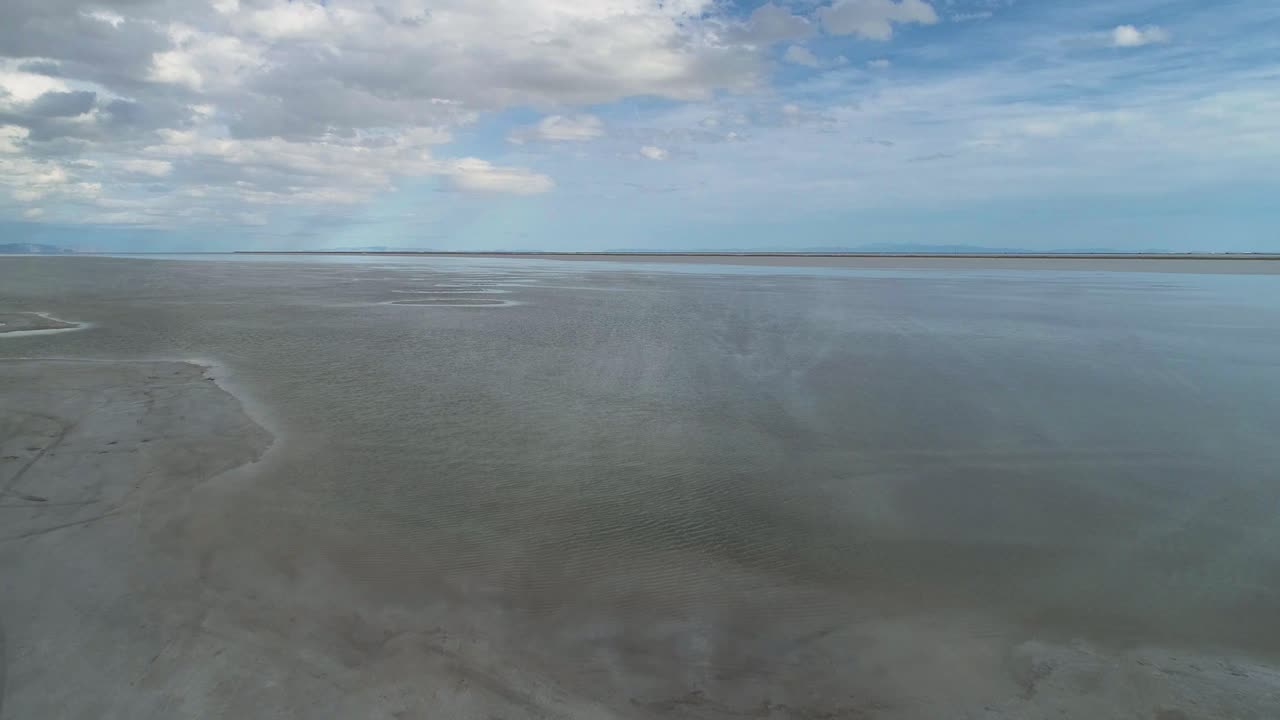 vuelo aéreo sobre grandes salinas con cielo nublado reflejándose en ellas