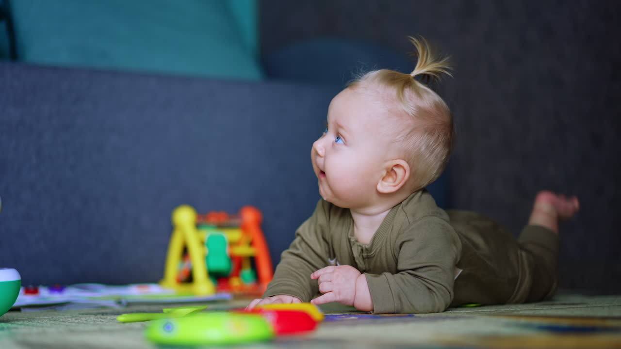 Blond child wearing sleepsuit crawls by the floor. Kid looks up with interest. Blurred backdrop.