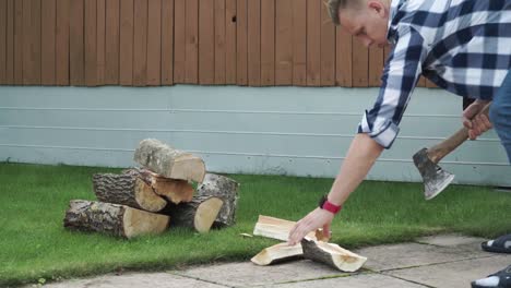Young man with blue checked shirt is chopping wood in smaller pieces