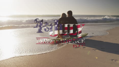 american flag waving over independence day text against couple sitting on surfboard on the beach