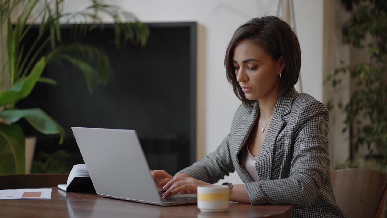 Portrait of Hispanic woman typing on laptop, sends an email to client and is happy with result. Businesswoman sitting at table