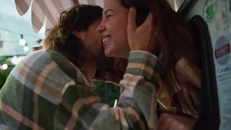 Happy-brunette-girl-looks-out-of-the-trailer-and-her-brunette-boyfriend-kisses-her-and-they-hug-during-their-picnic-outside-the-city-along-with-the-trailer-at-the-camp-in-the-summer