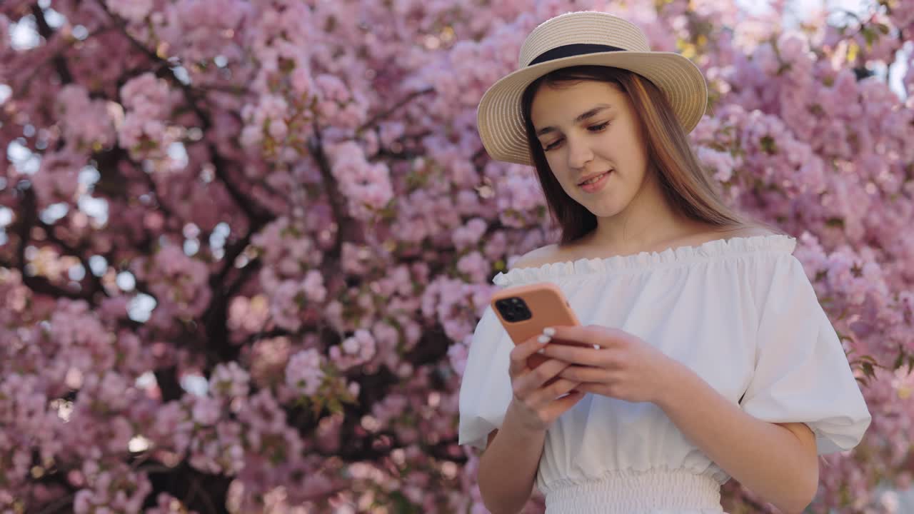 Teenage Girl Using Phone Under Cherry Blossom Trees