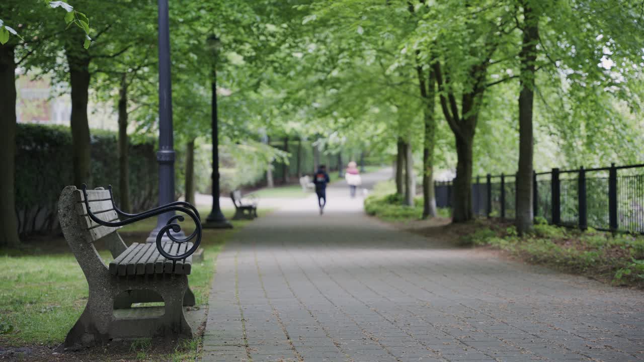 People walking in cobblestone path surrounded by trees and benches in Coal Harbour park area, Vancouver, British Columbia, Canada