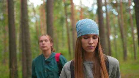 women hiking along forest trail, woman in gray sweatshirt appears tired, gazing forward determinedly, while her companion in green shirt glances around, softly blurred in background