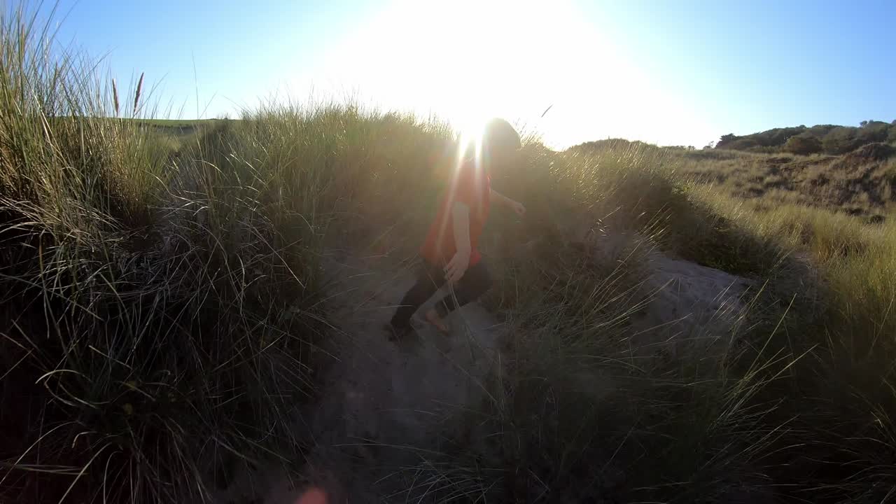 해변 휴가 에서 모래 언덕 을 가로질러 달리는 어린 소년 의 뒷면