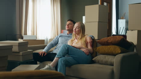 family relaxing new home couch looking on room interior with packed boxes.