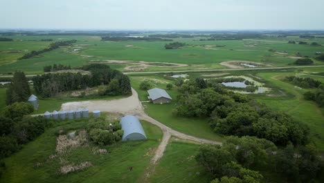 Lapso-De-Tiempo-Cinematográfico-órbita-De-Drones-Aéreos-Alrededor-Del-Oeste-De-Canadá-Pasto-Campo-Agricultura-Ganado-Granja-Casa-Contenedores-De-Granos-Y-Naturaleza-Paisaje-De-Campo-De-Pradera-Con-Carretera-Lago-Ribereño