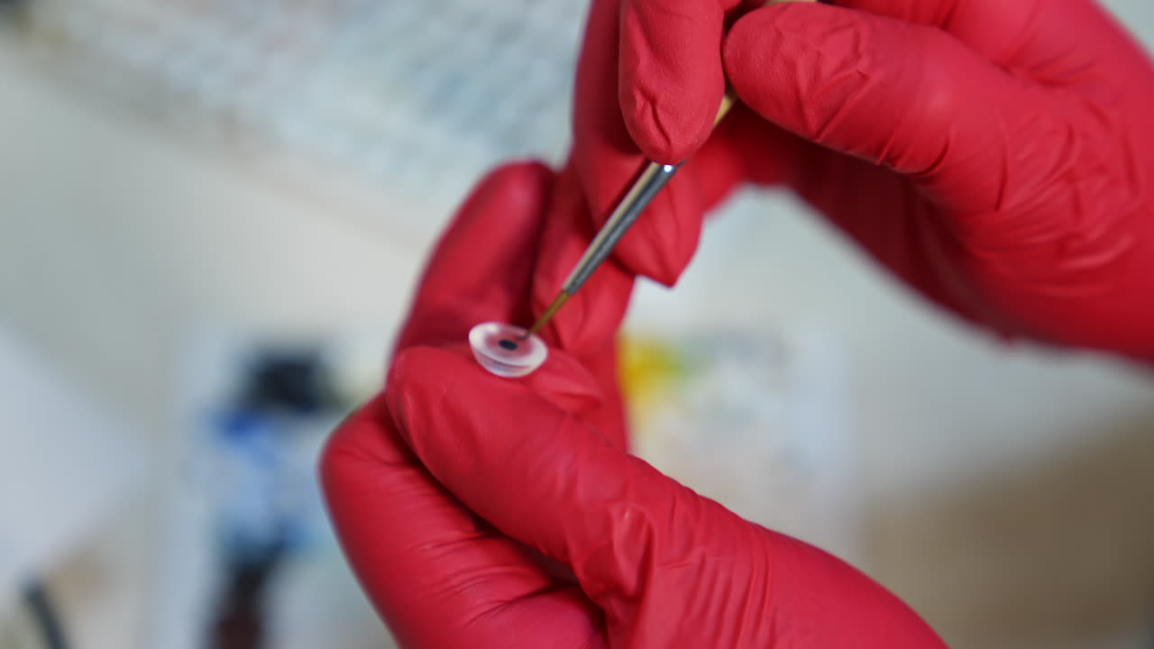 Making eye prosthesis in laboratory. Professional artist in medical gloves painting artificial eye with a brush. Ophthalmology concept. Close-up.