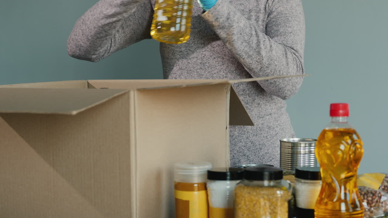 보호복을 입은 남자가 골판지 상자에 식료품 세트를 포장합니다.