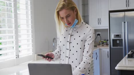 Mujer-Usando-Computadora-Portátil-Y-Teléfono-Inteligente-En-La-Cocina