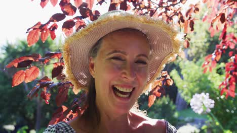 retrato de una mujer mayor caucásica feliz en el jardín con sombrero de sol y sonriendo al sol