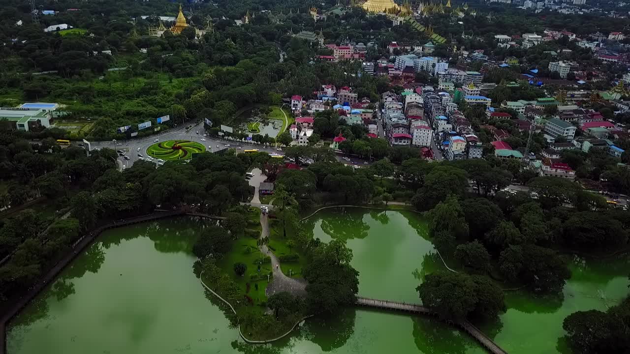 A breathtaking rising aerial over Kandawgyi Lake, Yangon, Myanmar, revealing the iconic Shwedagon Pagoda and the U Htaung Bo roundabout. Perfect for showcasing the city's landmarks and natural beauty