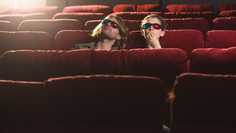 distant view of couple wearing 3d glasses sitting in the cinema while they watching a movie and eating popcorn 1