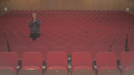 a tall white guy is in an empty theatre. he is the only one watching the show and the rest of chairs are empty. he stands up and starts to clap because he enjoys what he sees on stage