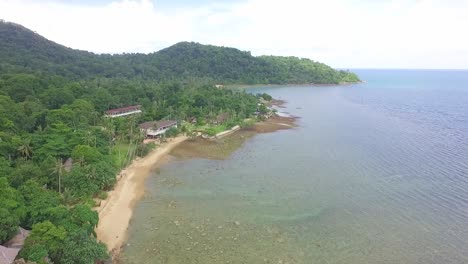 Toma-Aérea-Inclinándose-Hacia-Arriba-De-Una-Pequeña-Playa-Tropical-Con-Un-Pequeño-Hotel