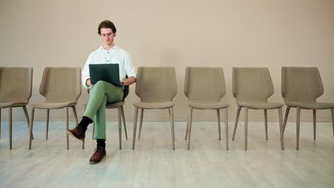 man sitting in an office waiting room using a laptop