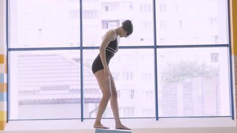 full body side shot of a girl putting on her swimming goggles before getting into the pool