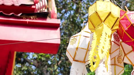 close-up of yellow and white lanterns hanging beneath a red roof with trees in the background.