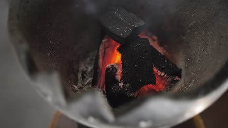 Primer-Plano-De-Pequeños-Carbones-Ardientes-Con-Calor-Rojo-Brillante-En-El-Centro-En-Un-Pequeño-Quemador-De-Incienso-En-Forma-De-Cuenco-Con-Humo-Blanco