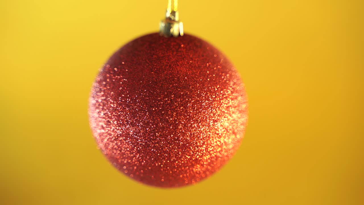 Close-up of a red glittering bal. Shiny Christmas red ball on yellow background. close up