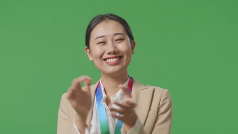 close up of asian business woman wearing a gold medal and clapping hands being proud winning as the first winner on green screen background in the studio