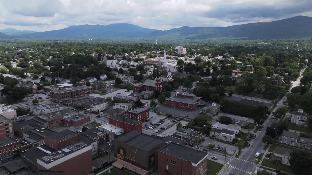 Wide drone shot of downtown Rutland Vermont in summer, with a church and mountains in the background