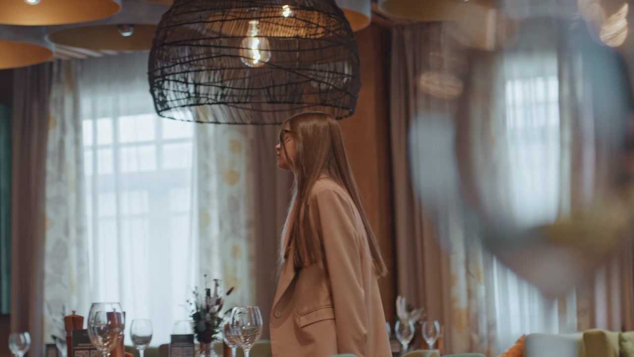 Donna caucasica seduta in un elegante bistrò, che guarda fuori dalla finestra, vino sul tavolo, capelli intrecciati, blazer neutro, luce soffusa della tenda, tavolo di legno lucido, scaffali decorativi, umore calmo e riflessivo, in attesa.