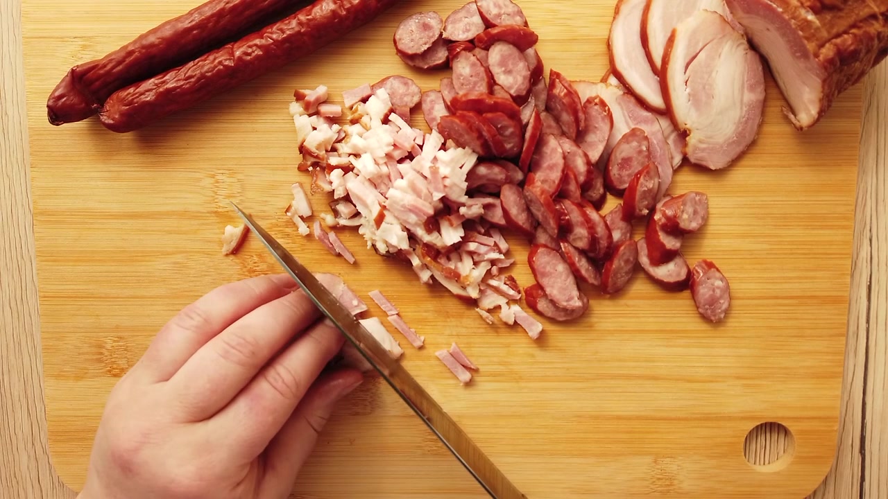 Il cuoco taglia salsiccia affumicata con pancetta su un tagliere