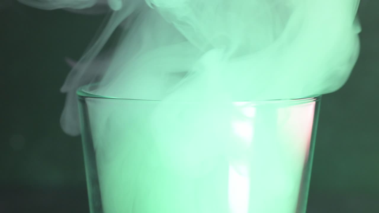 primer plano de un humo vertiendo en un vaso con luz verde