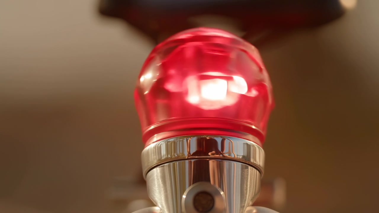 Vista ravvicinata dal basso e centrata che mostra una cupola traslucida rossa lucida posizionata su un connettore in cromo lucido, con brillanti riflessi speculari e rifrazioni interne mutevoli sulla plastica liscia e curva.