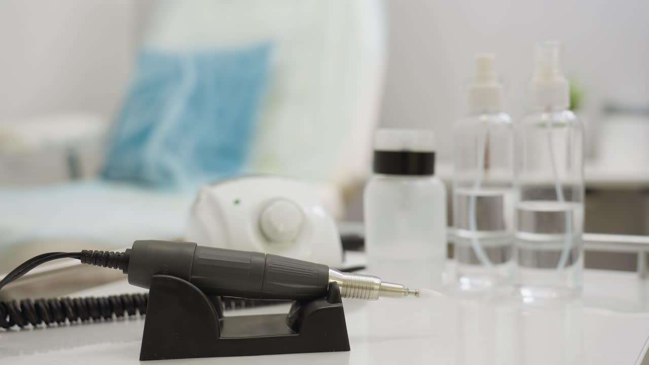Close-up of electric nail filer and cosmetic tools placed on white table with blurred background showing soft-focus indoor salon setting, creating clean and professional workspace atmosphere