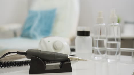 close-up of electric nail filer and cosmetic tools placed on white table with blurred background showing soft-focus indoor salon setting, creating clean and professional workspace atmosphere