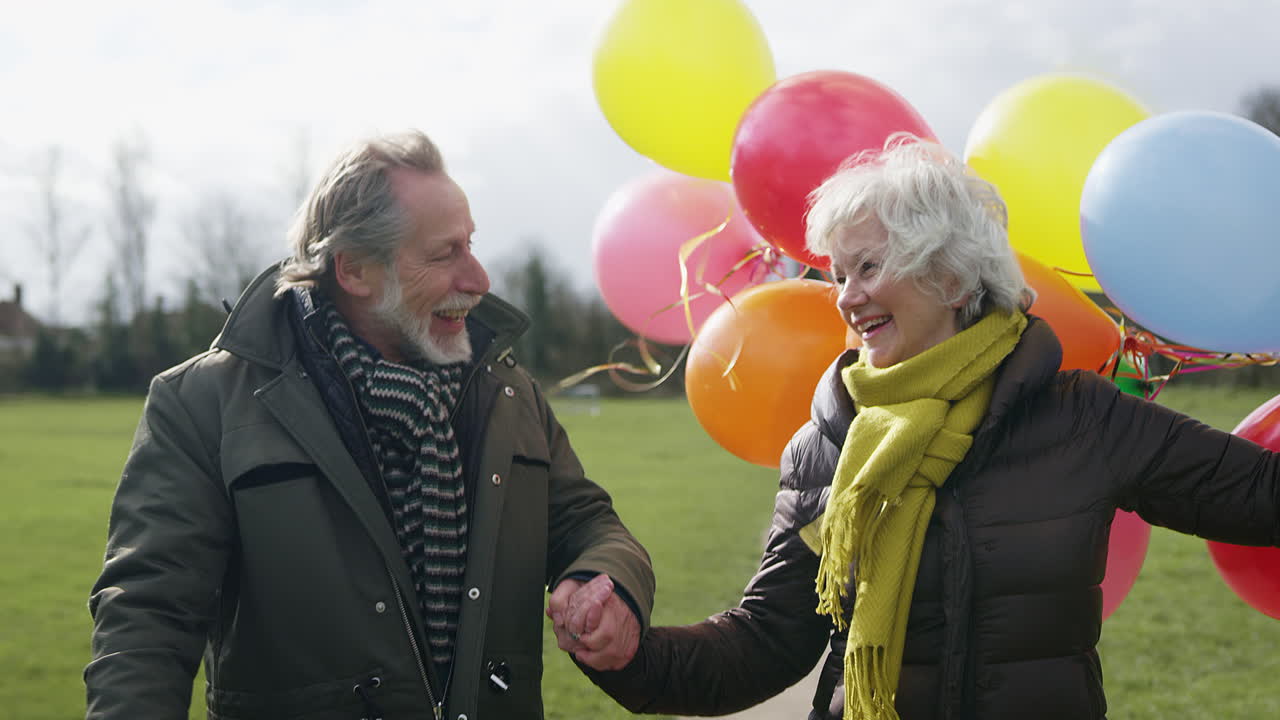 amorosa pareja de ancianos con globos disfrutando del otoño o el invierno caminando juntos por el parque