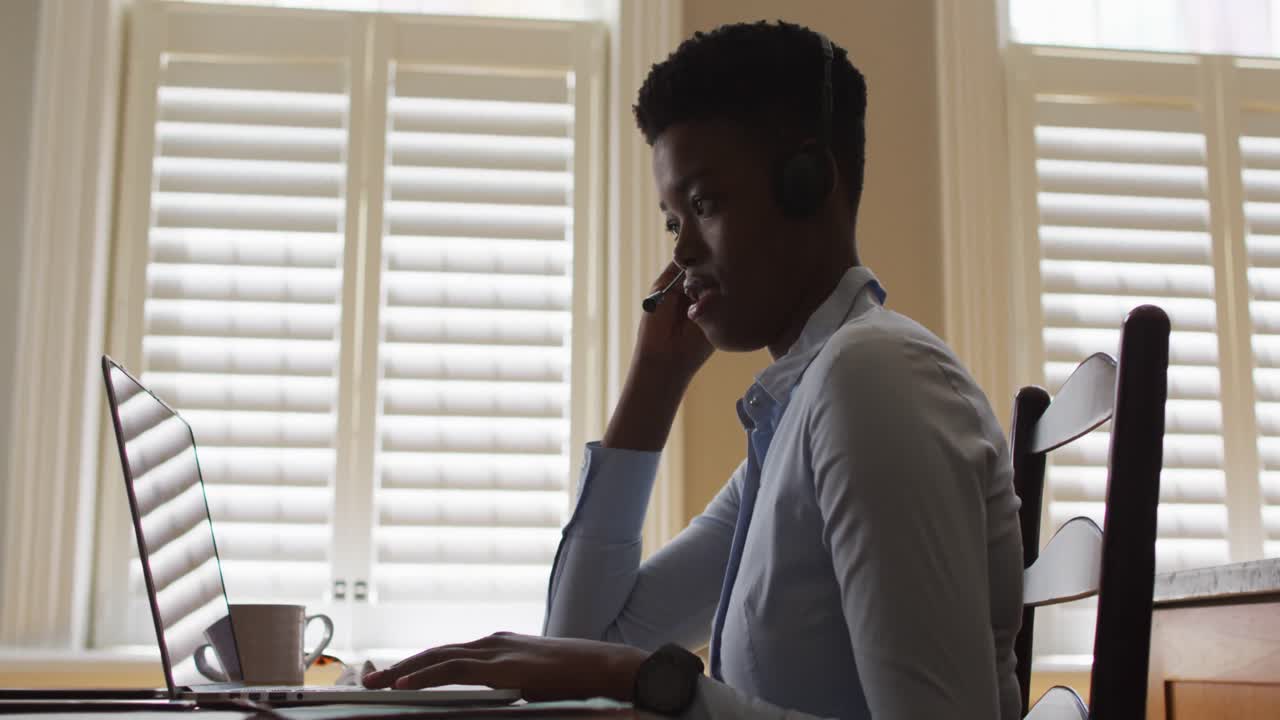 African american woman wearing phone headset having a videocall on laptop while working from home