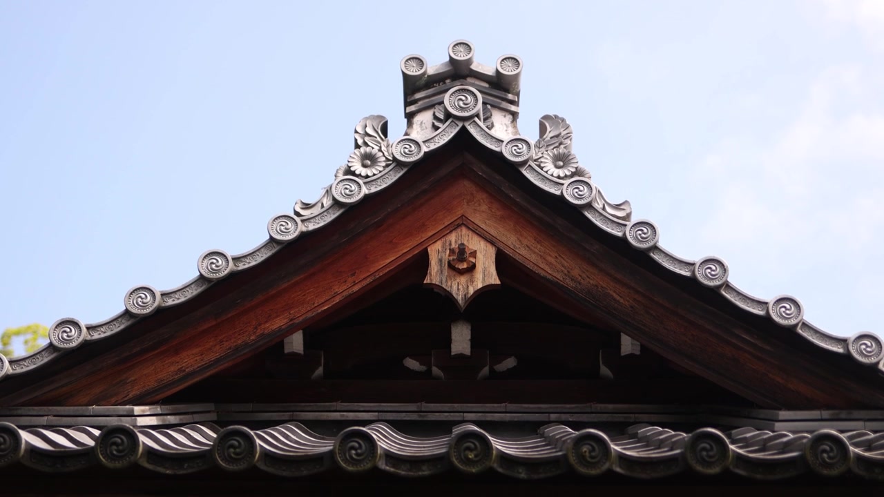Vista dettagliata dell'elegante tetto e del timpano decorativo del Tempio Nison-in ad Arashiyama, che evidenzia l'architettura buddista tradizionale giapponese contro un cielo pallido di Kyoto