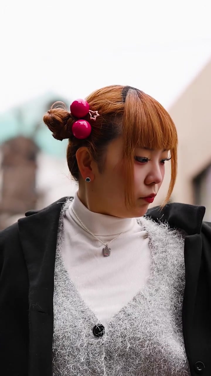 En stilfuld japansk kvinde med lyserøde håraccessories justerer sin sorte frakke i Harajuku, Tokyo.