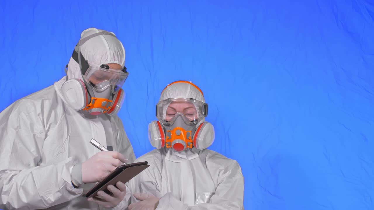 인공호흡기에서 바이러스학자 과학자는 태블릿 컴퓨터에 스타일러스를 사용해 글을 쓴다. 보호 의료 마스크를 착용한 남성과 여성, 크로마 키 블루.